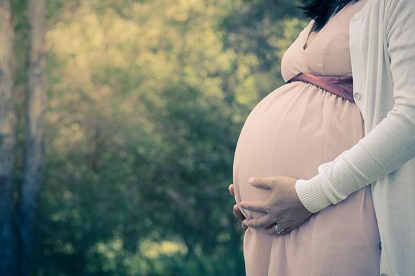 Close up of a woman in a beige dress holding her stomach outside