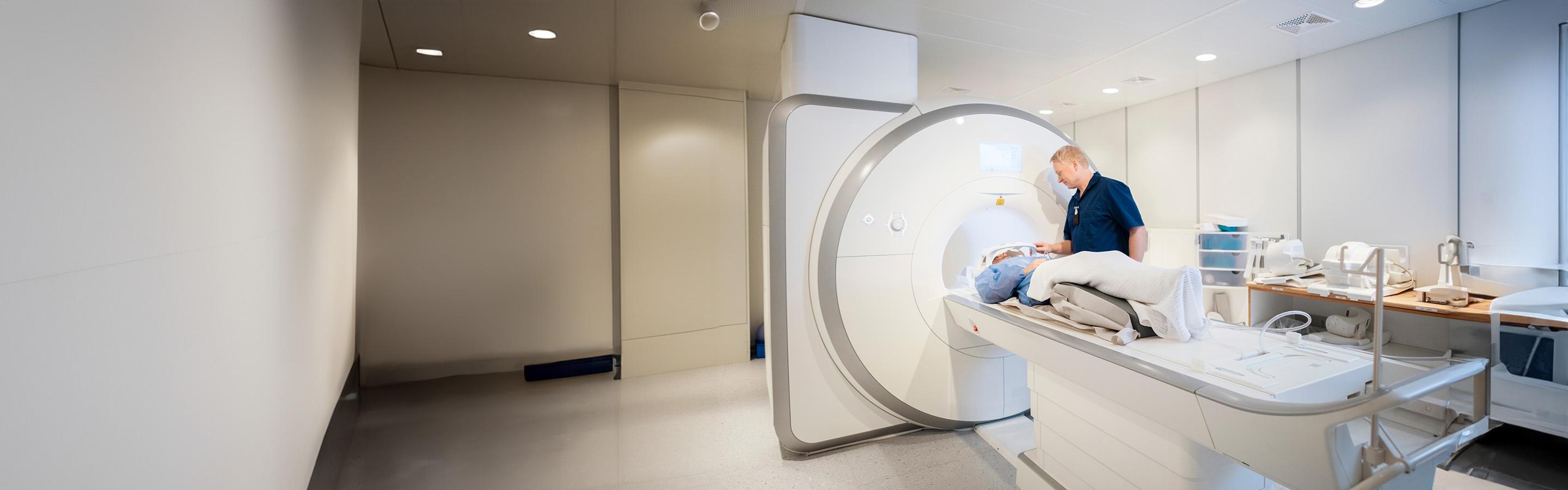 Female patient lying on a flat bed being moved into an MRI scanner by a radiographer