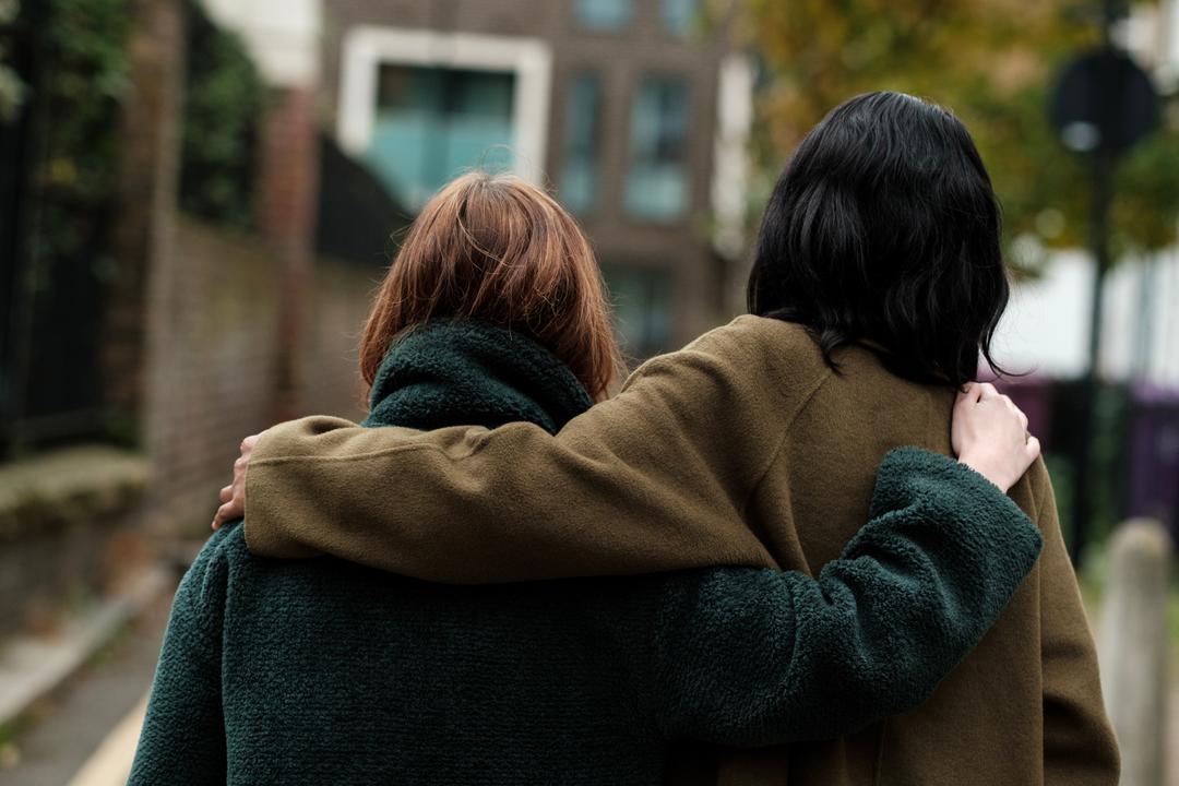 Two people holding onto each other as they walk down the street