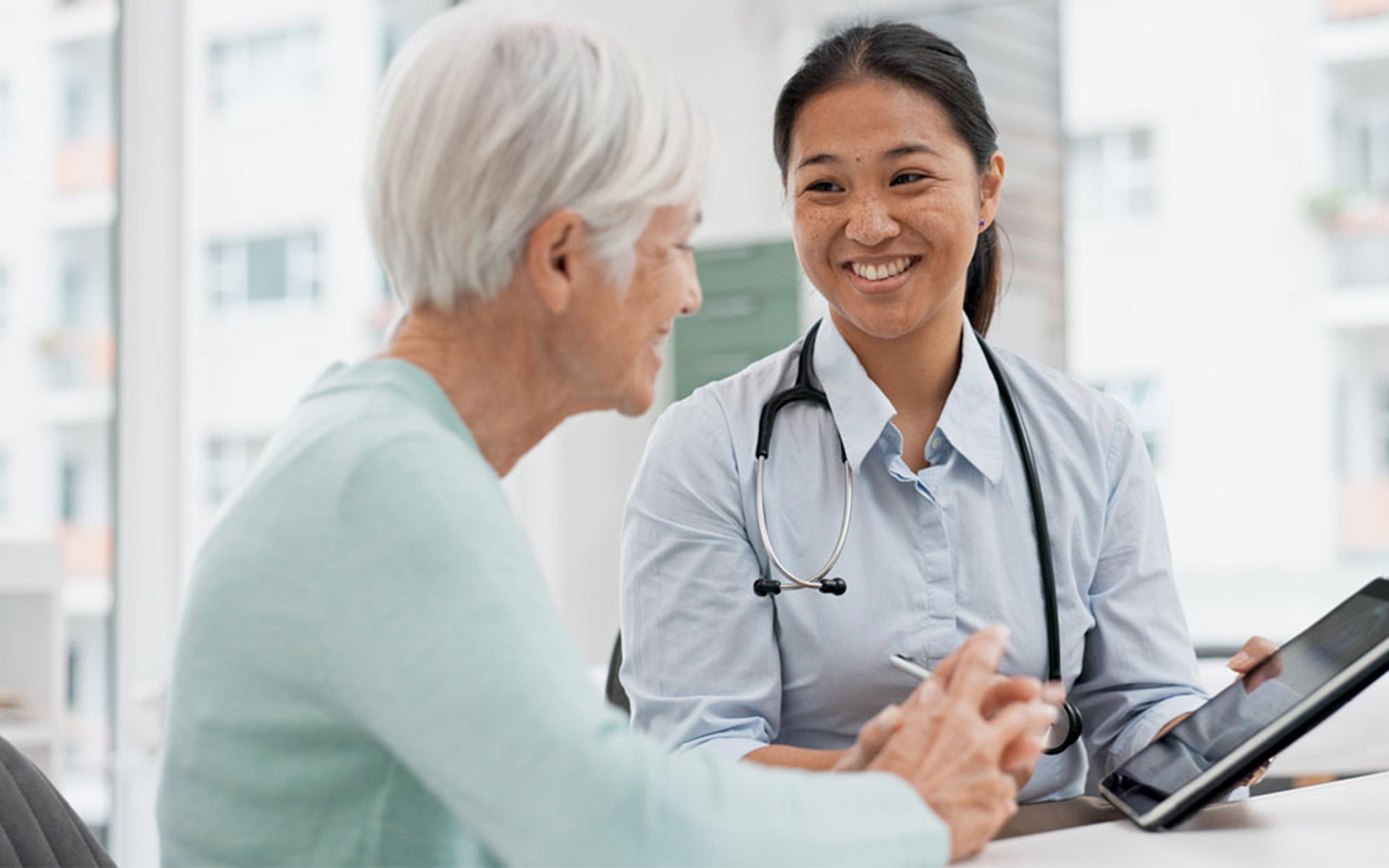 Smiling medical professional sharing updates on a tablet device with an elderly woman