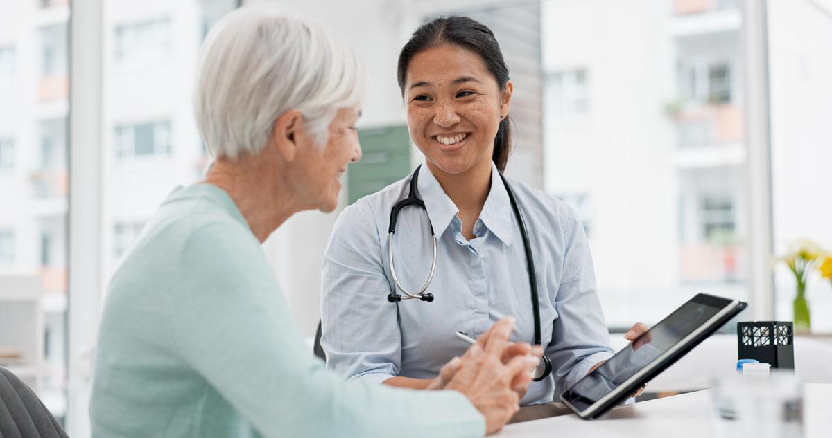 Smiling medical professional sharing updates on a tablet device with an elderly woman