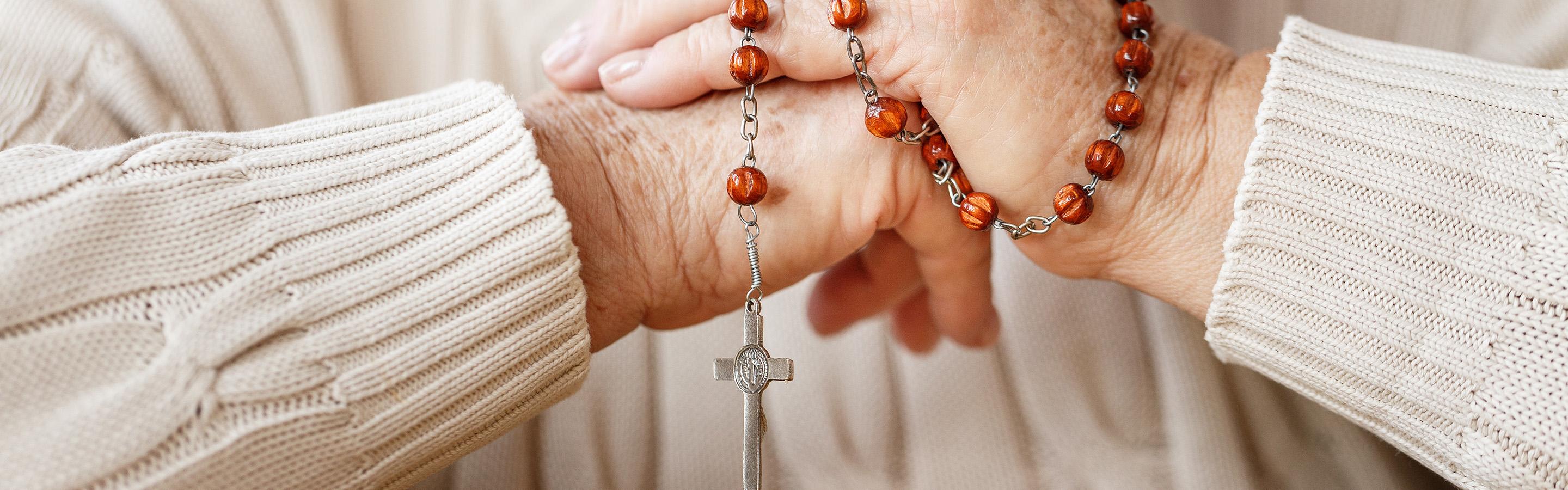 Senior woman with rosary beads wrapped around her hands.
