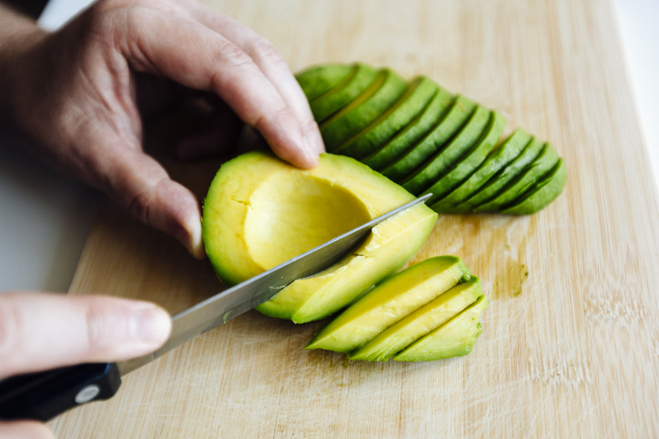 Man slicing avocado with a knife on a cutting board close up