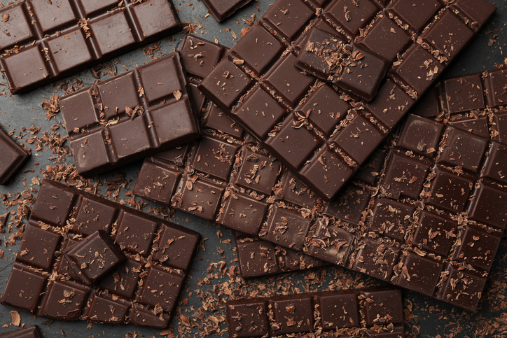 Pieces and shavings of tasty chocolate bars on grey table, flat lay